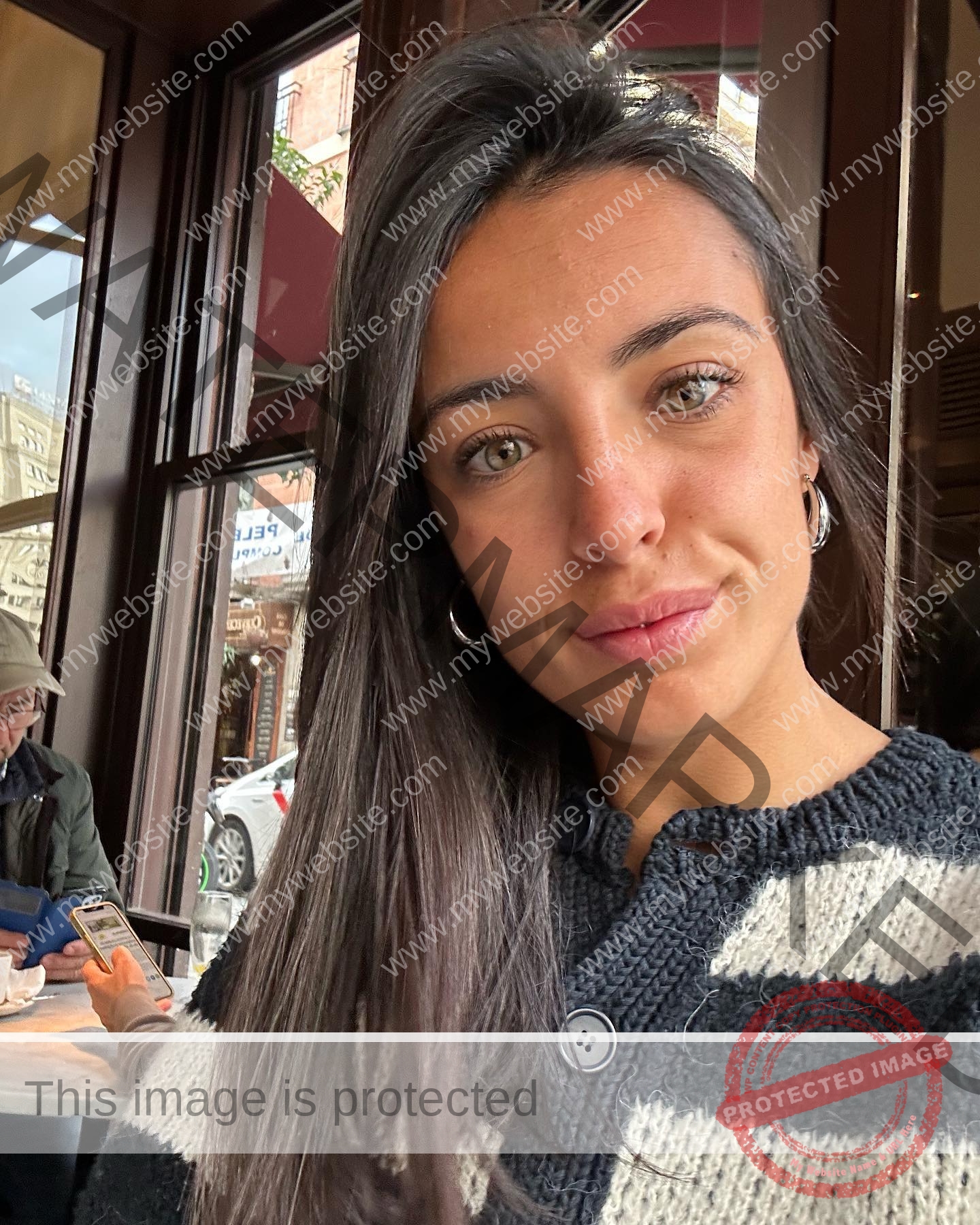 ainhoa-idoiaga-spain-ainhoidoiaga-00319 Ainhoa Idoiaga, track athlete from Spain, takes a selfie indoors in a striped sweater; someone uses a phone at a table behind her.