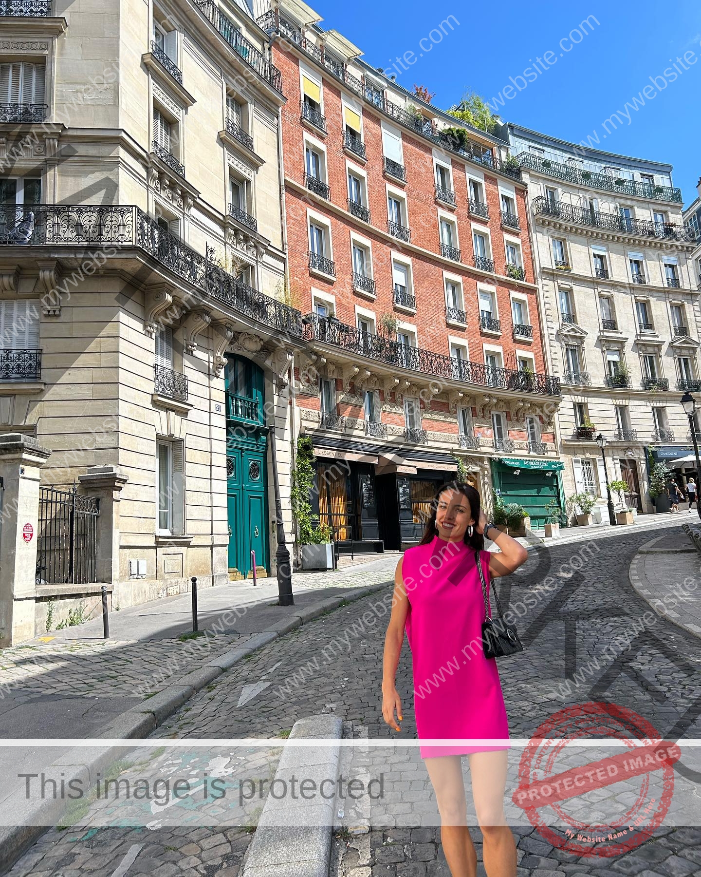 ainhoa-idoiaga-spain-ainhoidoiaga-00334 Ainhoa Idoiaga, track athlete from Spain, stands smiling in a bright pink dress on a cobblestone street with historic buildings and blue sky.