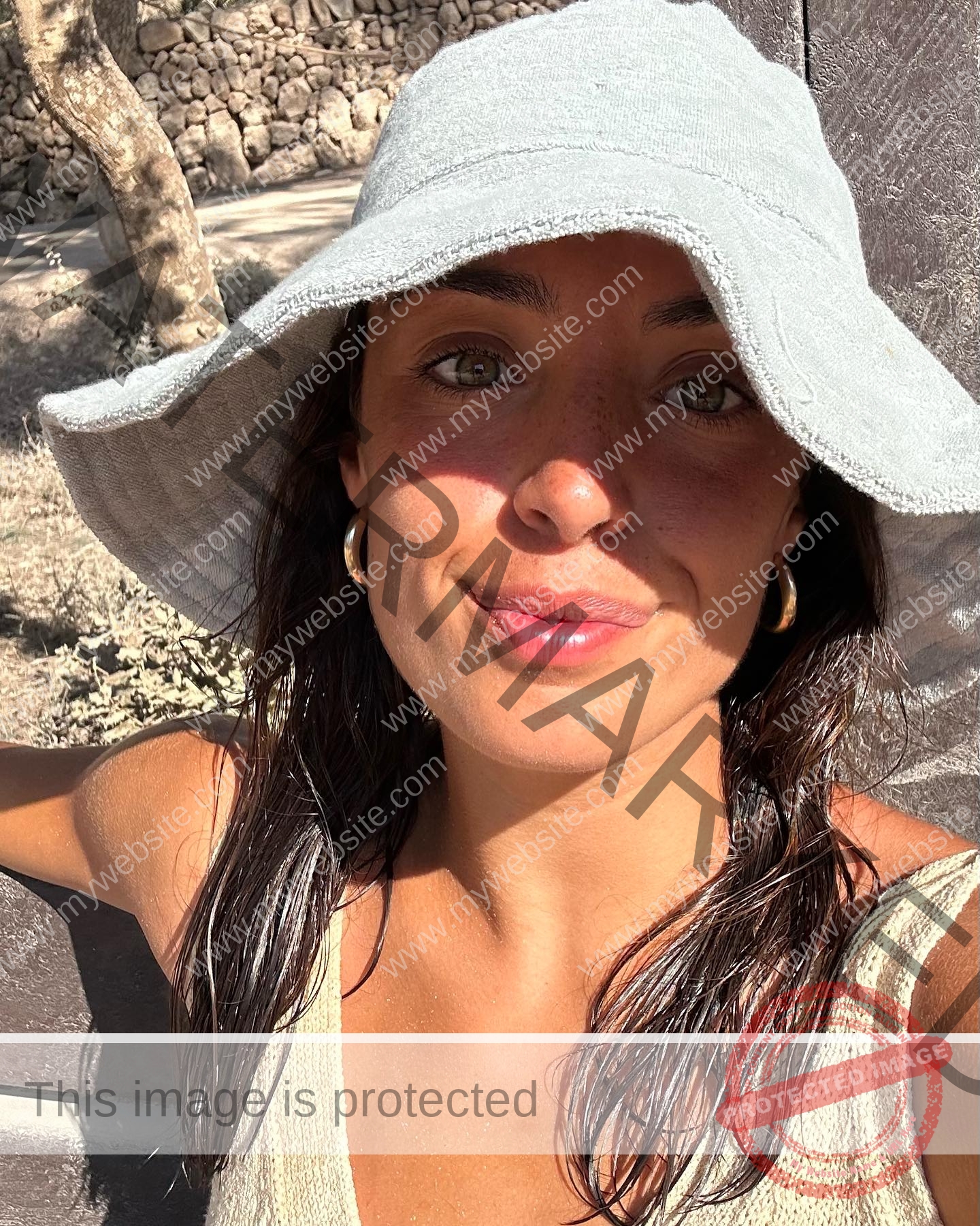 ainhoa-idoiaga-spain-ainhoidoiaga-00337 Ainhoa Idoiaga, track athlete from Spain, smiles in bright sunlight wearing a gray hat, beige tank top, with a wall and tree behind.