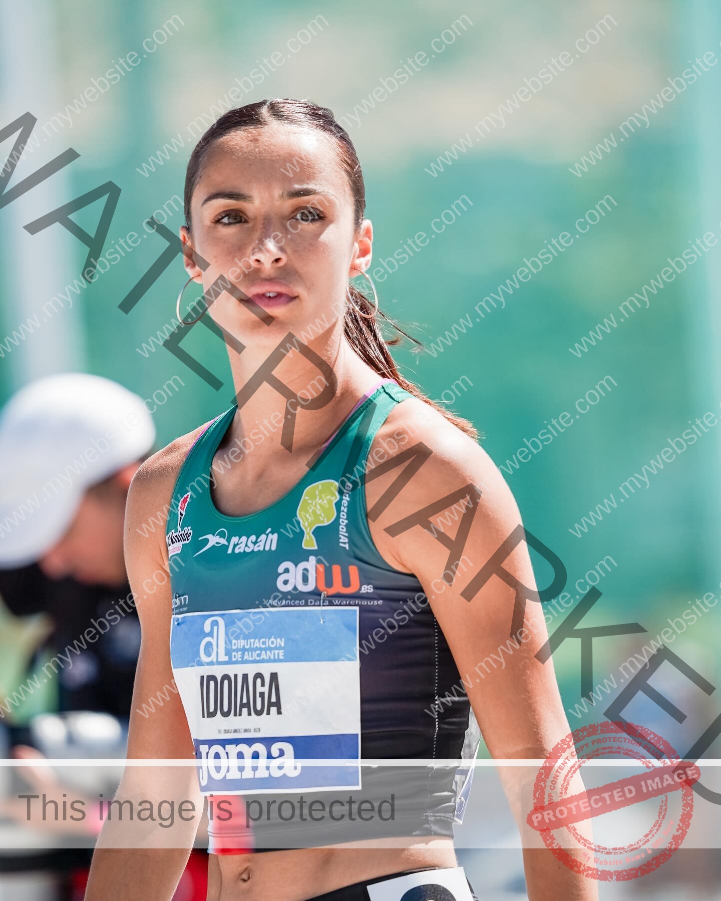 ainhoa-idoiaga-spain-ainhoidoiaga-00385 Ainhoa Idoiaga, track athlete from Spain, with dark hair in a ponytail, green-black sports top, hoop earrings, looking focused.