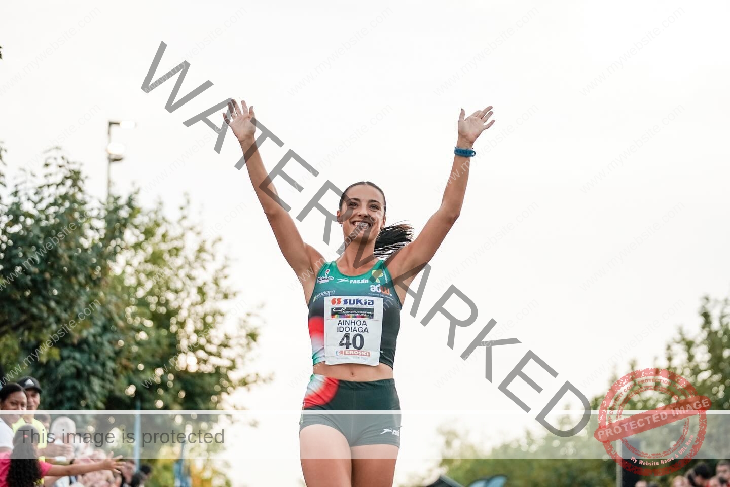 ainhoa-idoiaga-spain-ainhoidoiaga-00399 Ainhoa Idoiaga, track athlete from Spain, in running gear with bib 40, smiles and lifts arms in victory at an outdoor race.