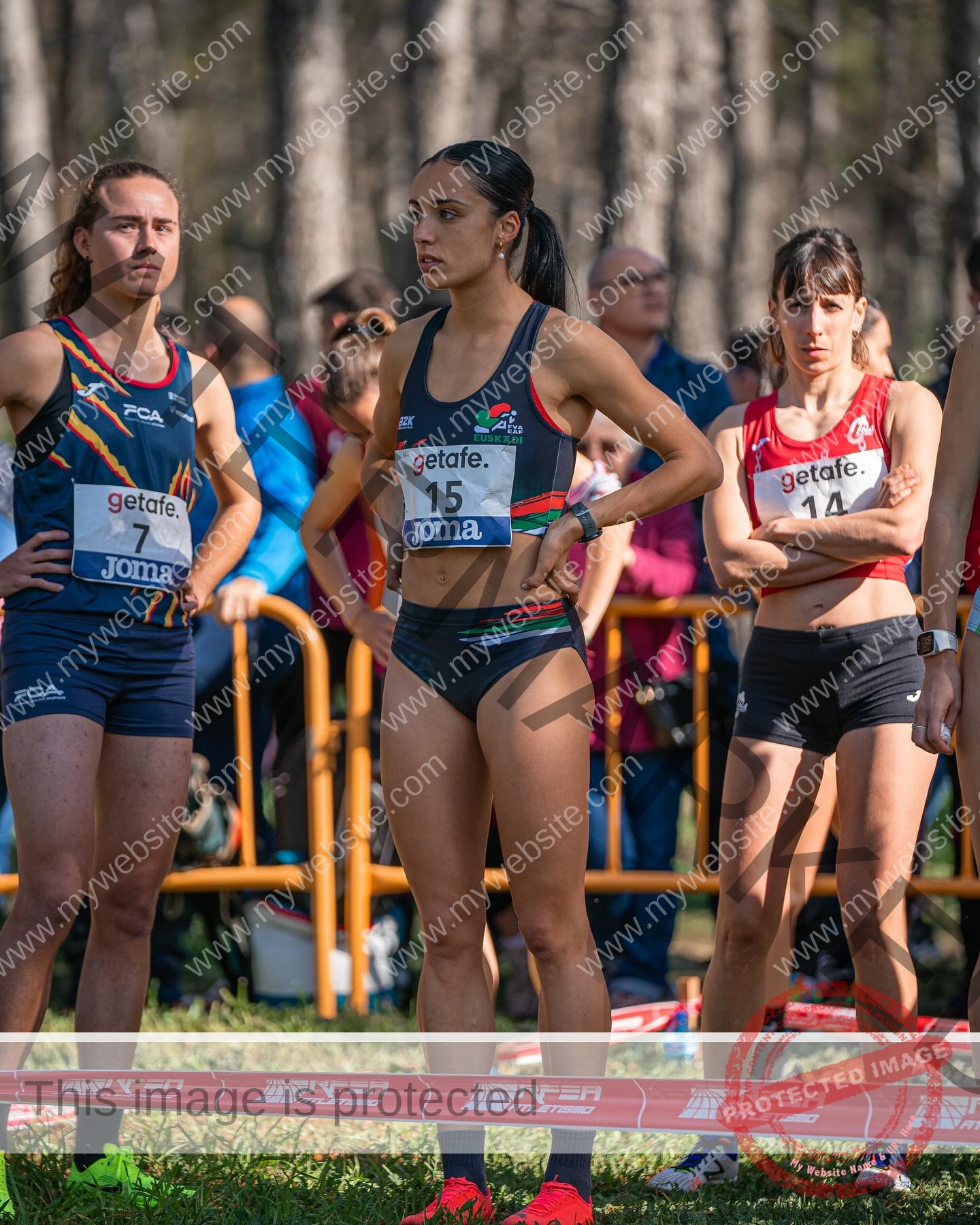 ainhoa-idoiaga-spain-ainhoidoiaga-00406 Ainhoa Idoiaga, track athlete from Spain, stands with two other female runners at the outdoor start line, wearing bib number 15.
