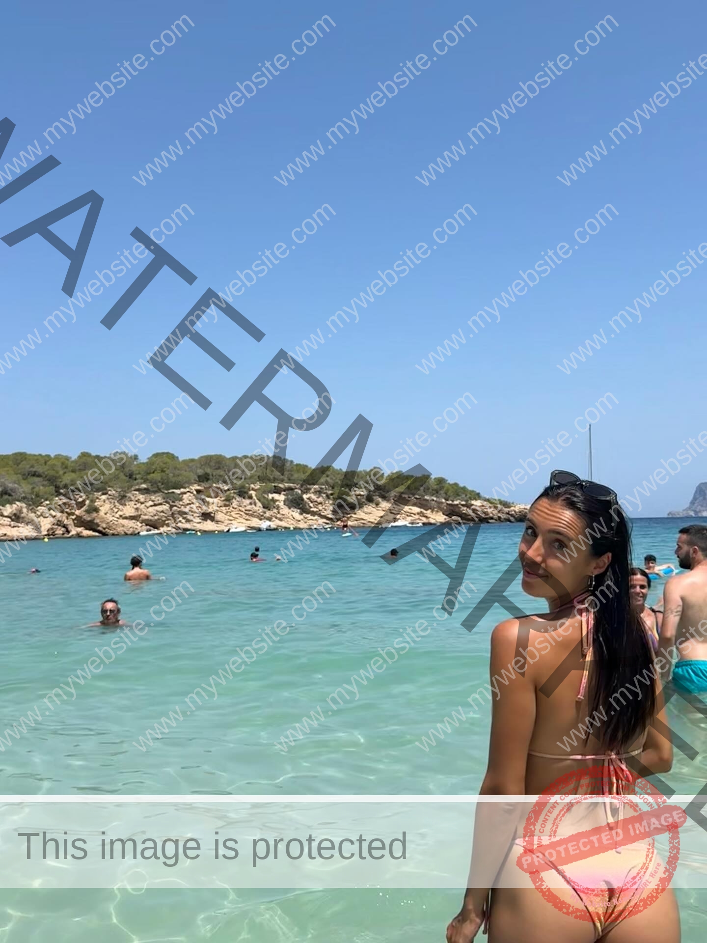 ainhoa-idoiaga-spain-ainhoidoiaga-00469 Ainhoa Idoiaga, track athlete from Spain, stands in pink bikini in clear shallow water at a beach, looking back over her shoulder.