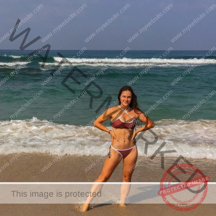 Alina Drutman Alina Drutman stands on a sandy Israeli beach, smiling in her bikini with waves behind and blue sky overhead.