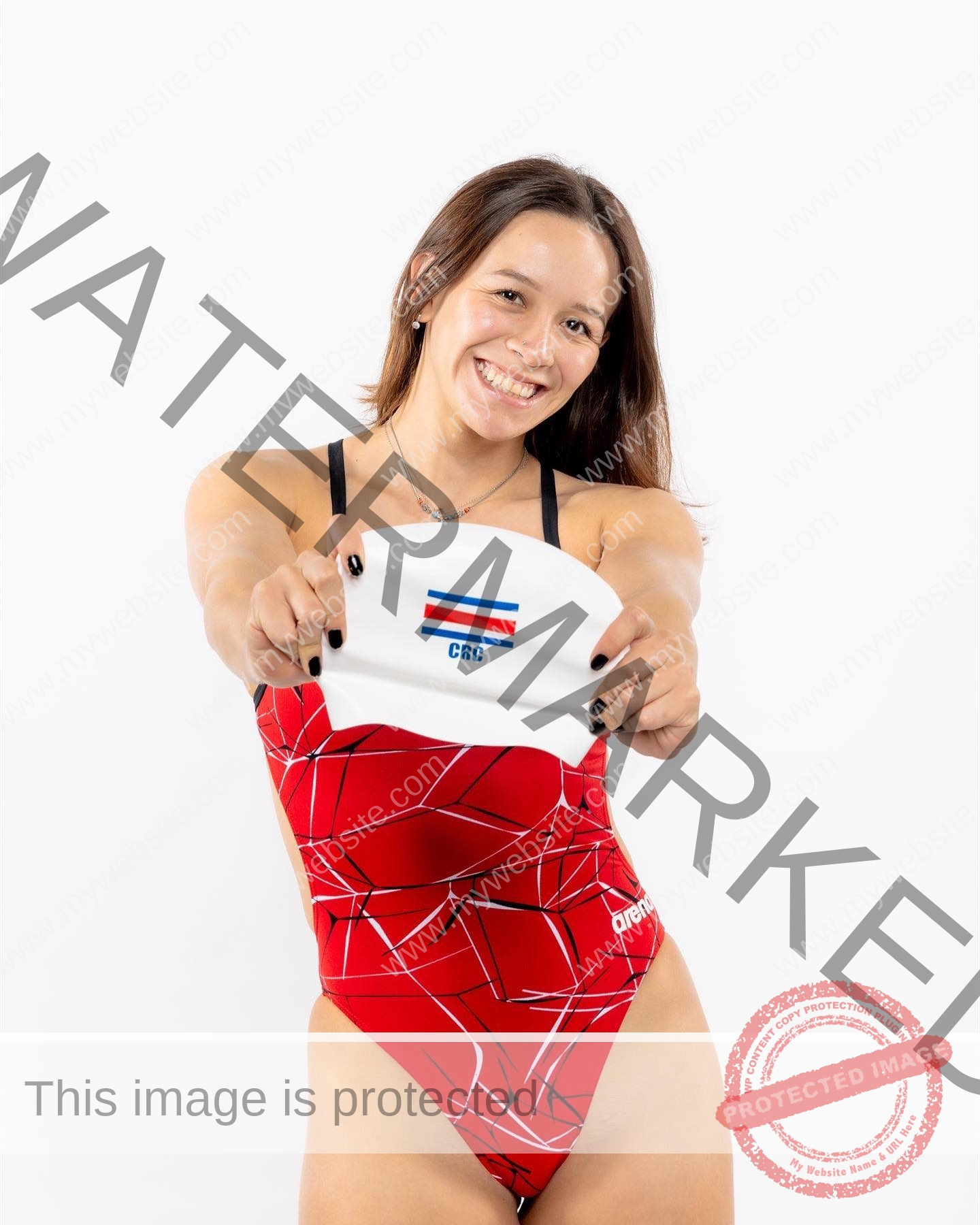 alondra-ortiz-costa-rica-alortizroman-458 Alondra Ortiz smiles in a red patterned swimsuit, holding a Costa Rican flag swim cap against a white background, proud champion.