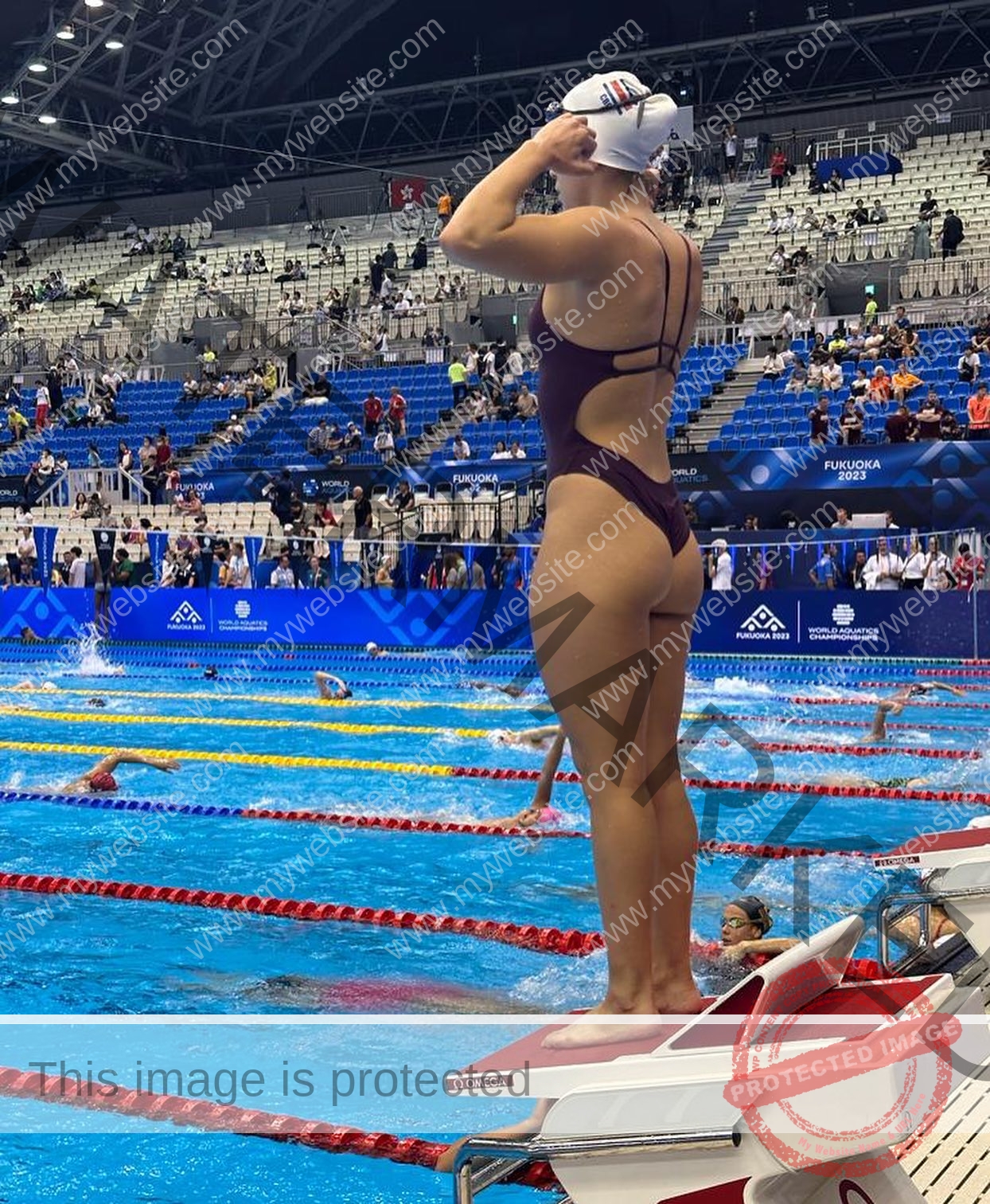 alondra-ortiz-costa-rica-alortizroman-521 Alondra Ortiz Costa Rican swimmer Alondra Ortiz, in a maroon swimsuit and white swim cap, stands on the starting block looking at the pool.