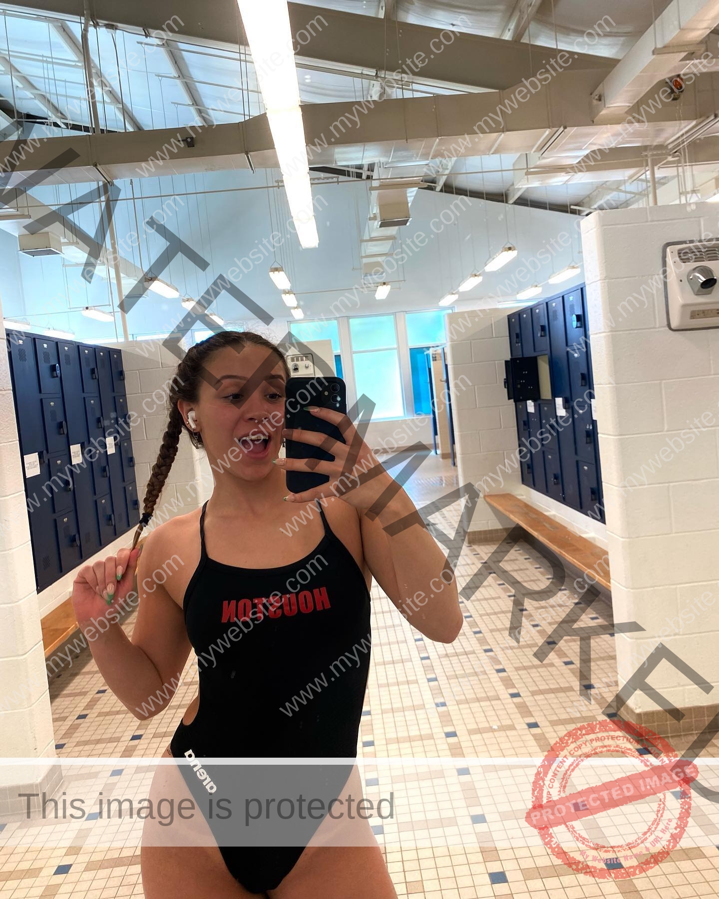 alondra-ortiz-costa-rica-alortizroman-549 Alondra Ortiz smiles in a black HOUSTON swimsuit, snapping a selfie in a blue-locker room, braid in hand on tiled floor.
