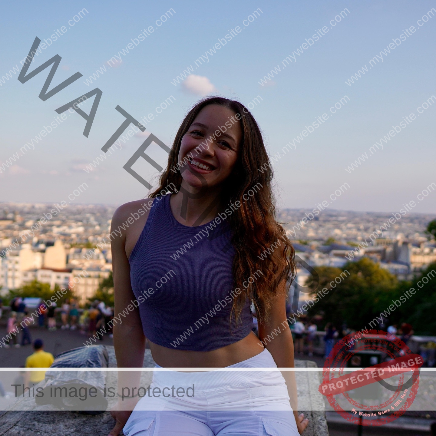 alondra-ortiz-costa-rica-alortizroman-660 Alondra Ortiz A young woman with long wavy hair, in a purple crop top and white pants, smiles on a ledge amid city crowds and trees.