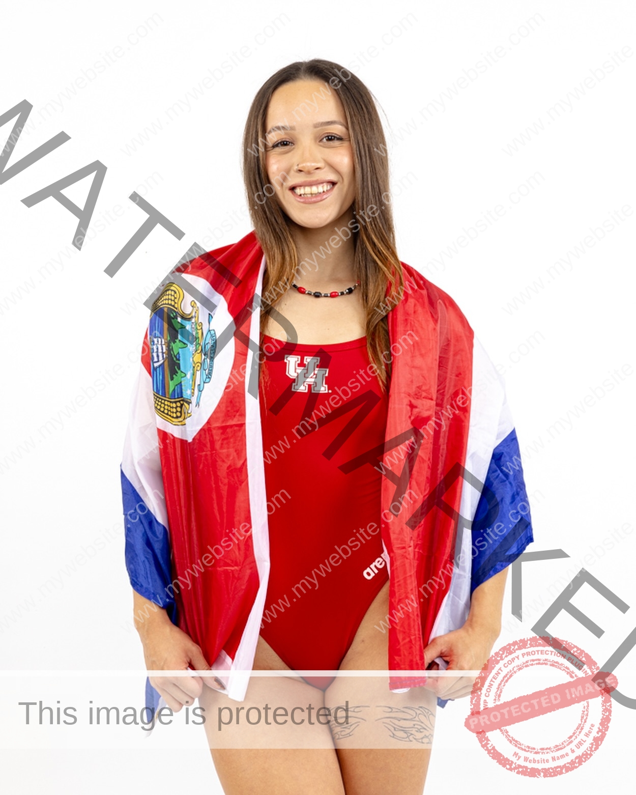 alondra-ortiz-costa-rica-alortizroman-664 Alondra Ortiz smiles in a red swimsuit and necklace, wrapped in a Costa Rica flag with crest, against a white background.