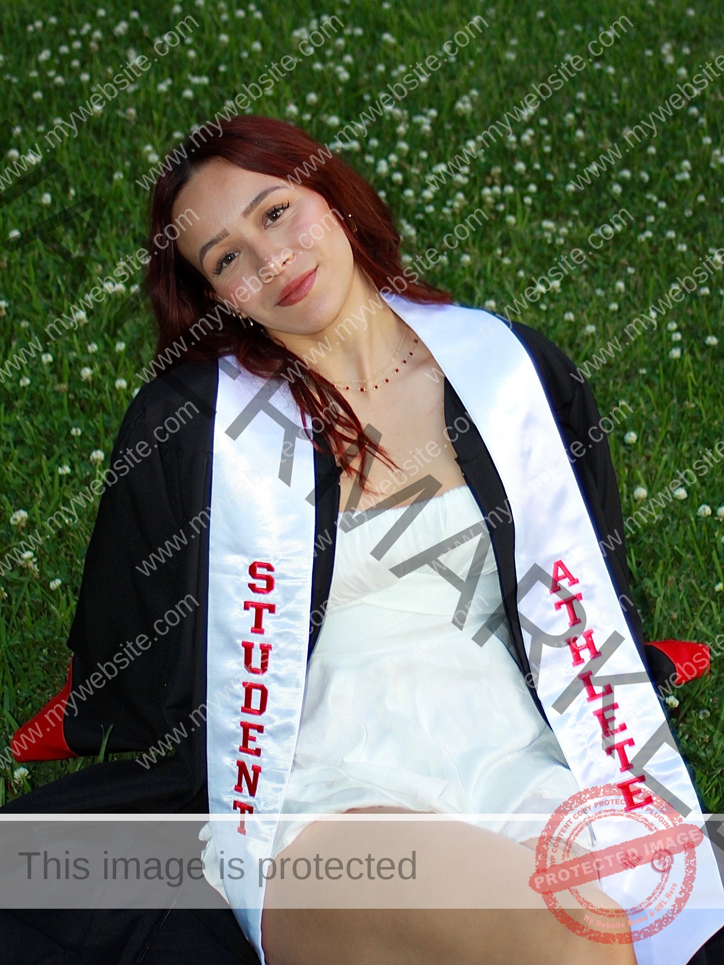 alondra-ortiz-costa-rica-alortizroman-687 Alondra Ortiz A young woman, Alondra Ortiz, in a graduation gown and white Student Athlete stole sits smiling on grass with white flowers.