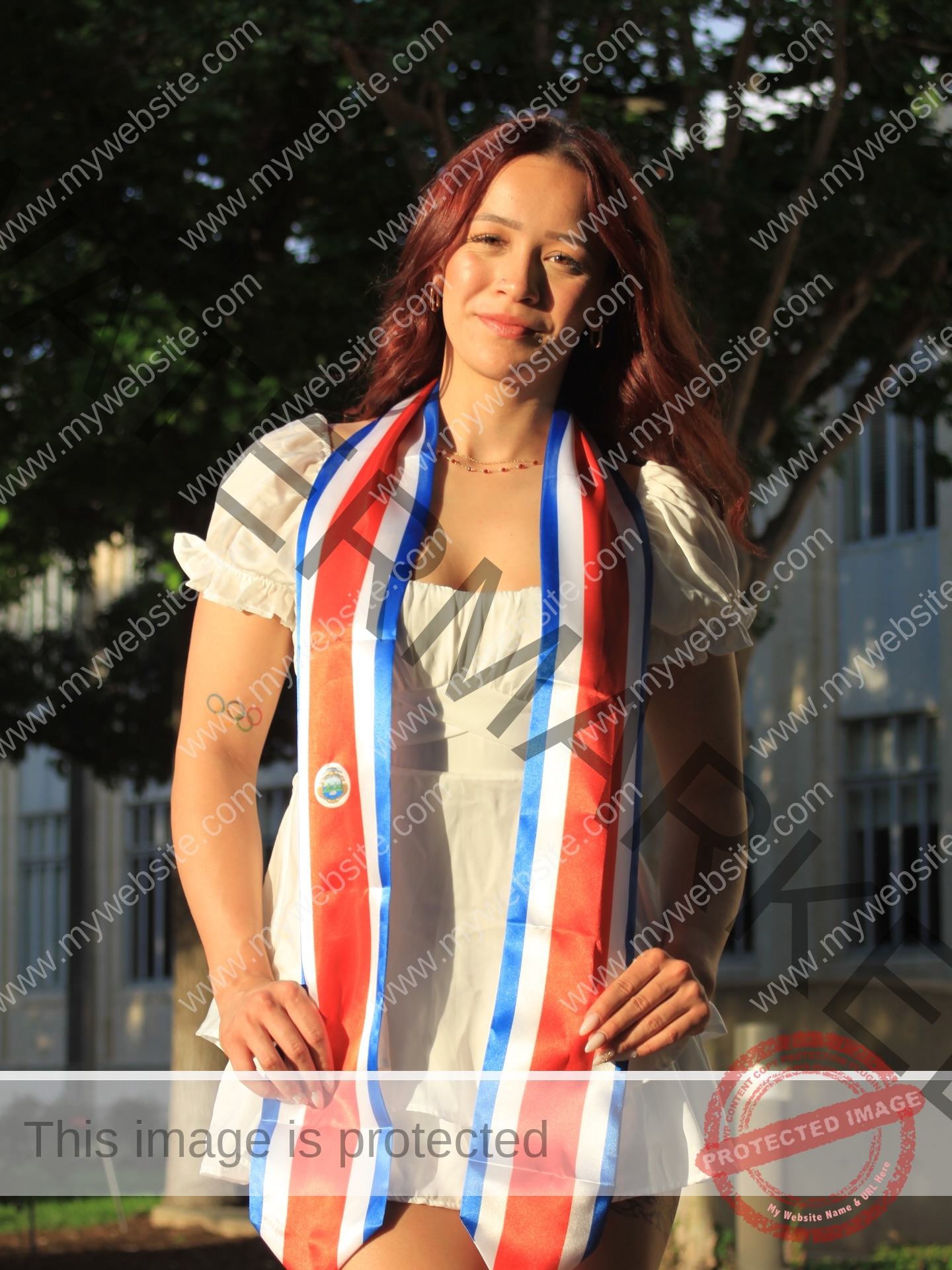 alondra-ortiz-costa-rica-alortizroman-689 Alondra Ortiz Alondra Ortiz, a swimming champion with long red hair, wears a white dress and patriotic stole, smiling outside by trees.