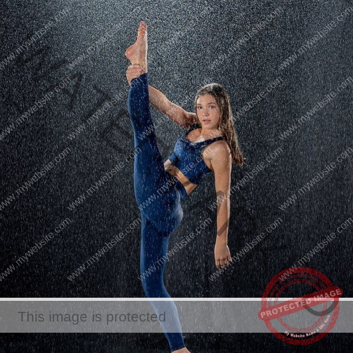 Amarae Krafka Amarae Krafka, a young woman in blue athletic gear, does a high leg stretch in falling water with a black backdrop.