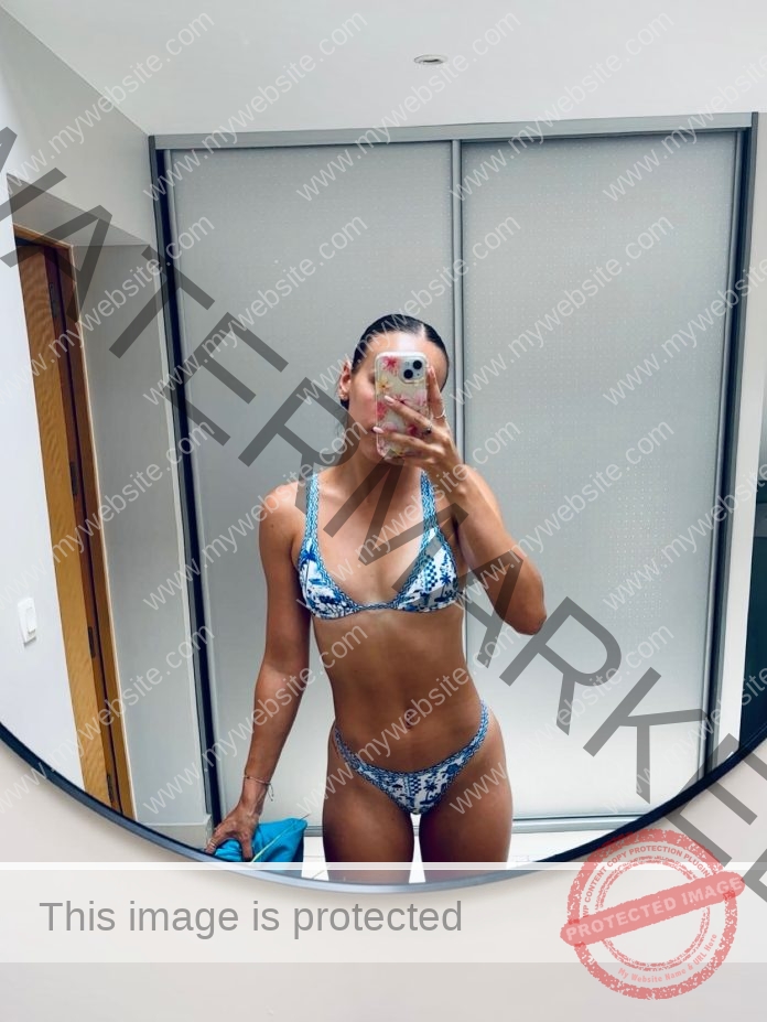 Anaelle Imbert, track star from France, in a blue and white bikini takes a mirror selfie in a modern room, face partly hidden by phone.