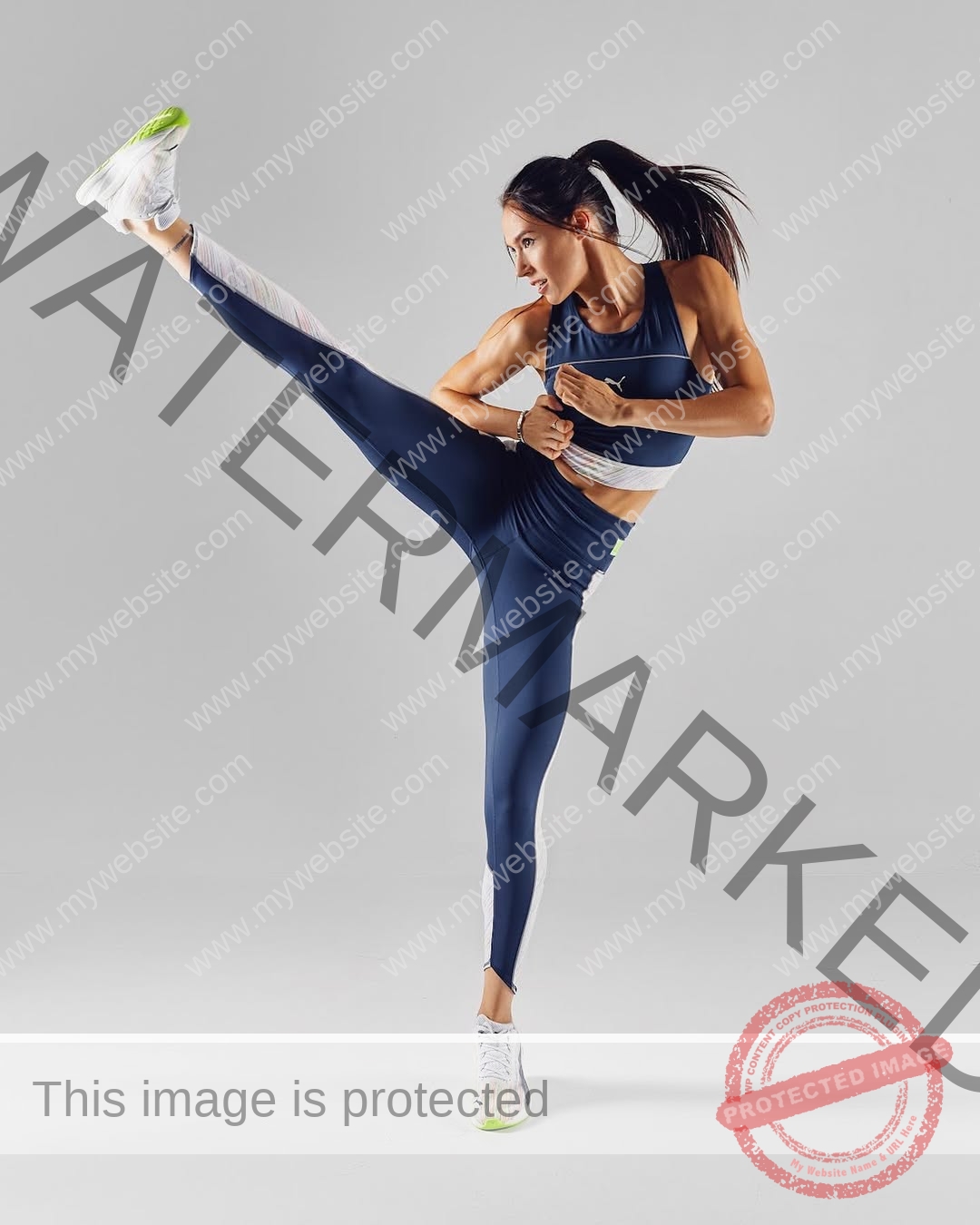 anastasia-bryzgina-ukraine-bryzgina_a-03941 Anastasia Bryzgina, track star from Ukraine, high kicks in navy blue athletic wear and white sneakers on a plain gray background.