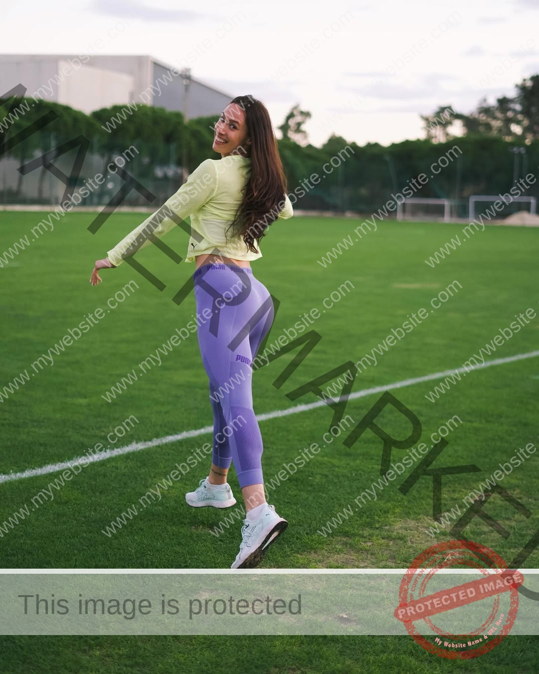 anastasia-bryzgina-ukraine-bryzgina_a-03978 Anastasia Bryzgina, track star from Ukraine, smiles in a light green top and purple leggings while walking on a grassy sports field.