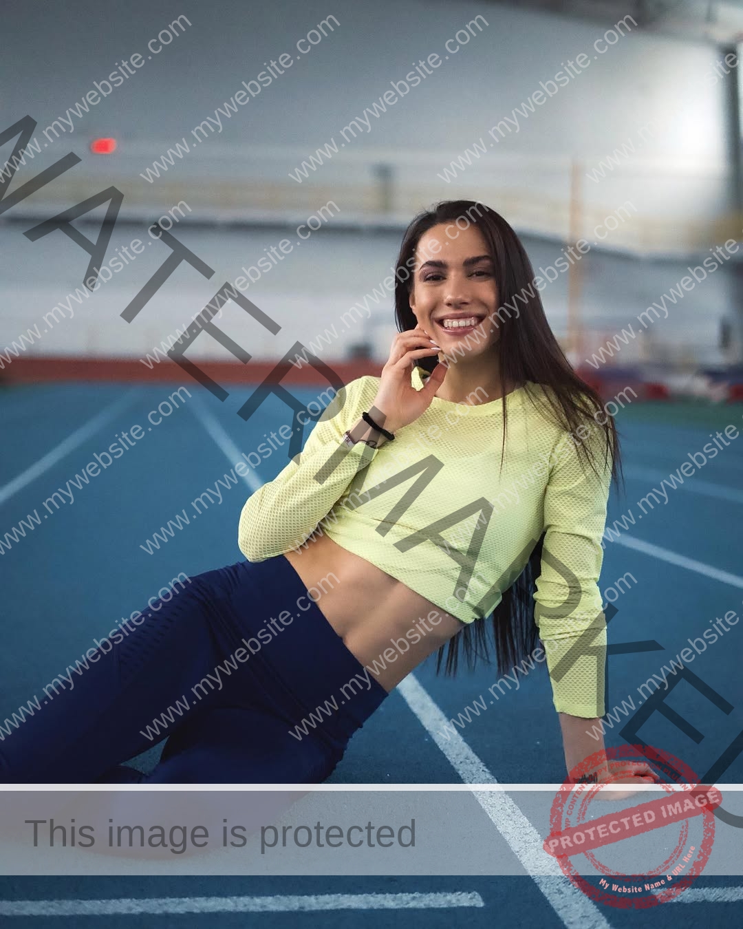 anastasia-bryzgina-ukraine-bryzgina_a-03984 Anastasia Bryzgina, track star from Ukraine, smiles in a yellow crop top and navy leggings while sitting on an indoor running track.
