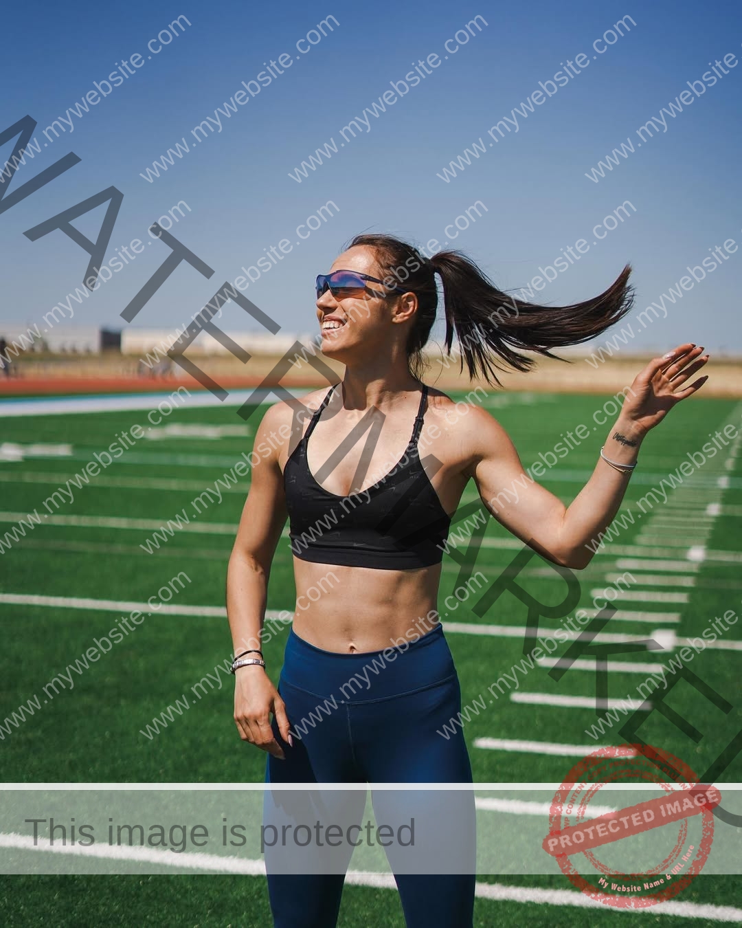 anastasia-bryzgina-ukraine-bryzgina_a-04030 Anastasia Bryzgina, track star from Ukraine, stands on a sunny track in a sports bra and blue leggings, smiling in sunglasses.
