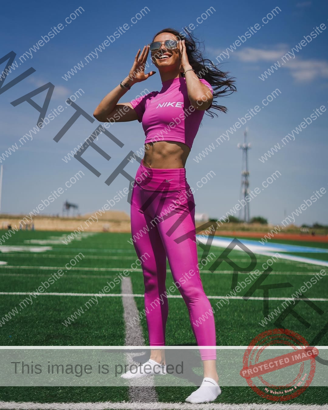 anastasia-bryzgina-ukraine-bryzgina_a-04033 Anastasia Bryzgina, track star from Ukraine, stands on a green field in bright pink Nike gear, smiling and adjusting sunglasses.