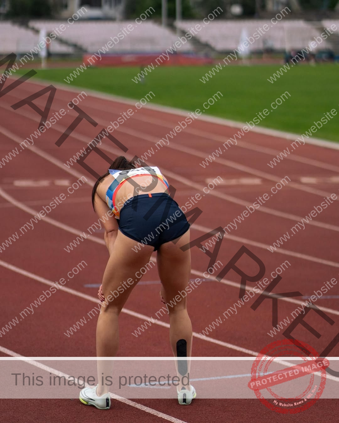 anastasia-bryzgina-ukraine-bryzgina_a-04113 Anastasia Bryzgina, track star from Ukraine, in running gear bends over on a red track catching her breath; stadium blurred behind.