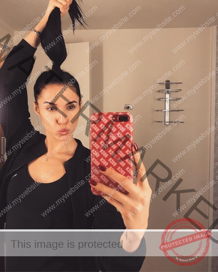 anastasia-bryzgina-ukraine-bryzgina_a-04114 Anastasia Bryzgina, track star from Ukraine, takes a mirror selfie in a bathroom, phone with red case, lips puckered, hair up.