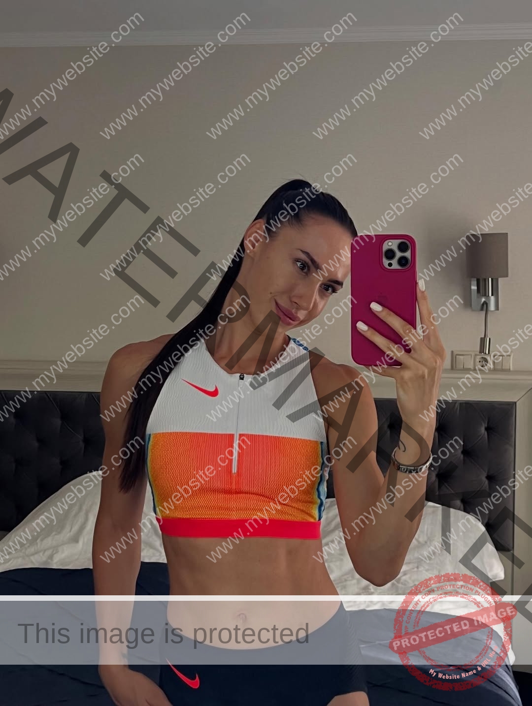 anastasia-bryzgina-ukraine-bryzgina_a-04119 Anastasia Bryzgina, track star from Ukraine, takes a mirror selfie in sporty gear, smiling and holding a pink phone by her bed.