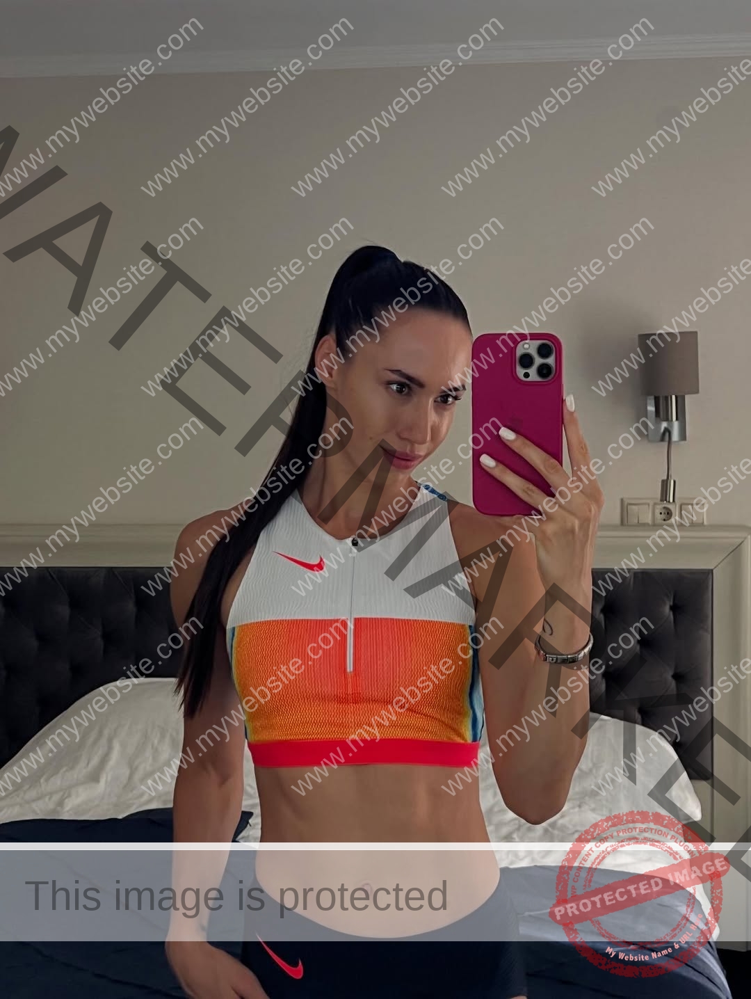 anastasia-bryzgina-ukraine-bryzgina_a-04120 Anastasia Bryzgina, track star from Ukraine, takes a mirror selfie in a bedroom in colorful crop top and black leggings, smiling.