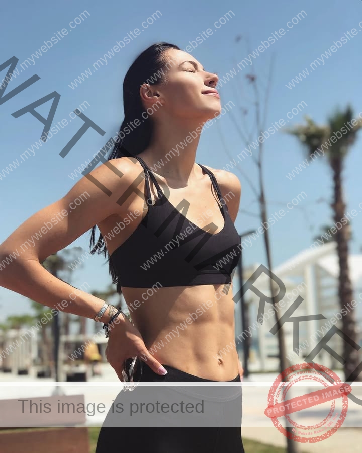 anastasia-bryzgina-ukraine-bryzgina_a-04128 Anastasia Bryzgina, track star from Ukraine, stands outdoors in athletic wear, eyes closed and smiling in the sun by palms and buildings.