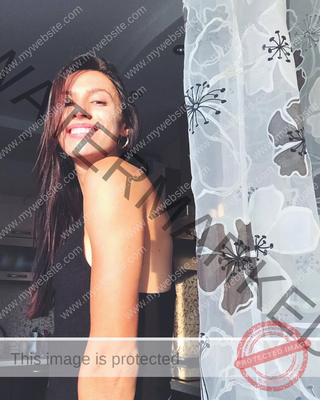 anastasia-bryzgina-ukraine-bryzgina_a-04142 Anastasia Bryzgina, track star from Ukraine, with long brown hair in a black top smiles near a sunlit window with floral curtains.