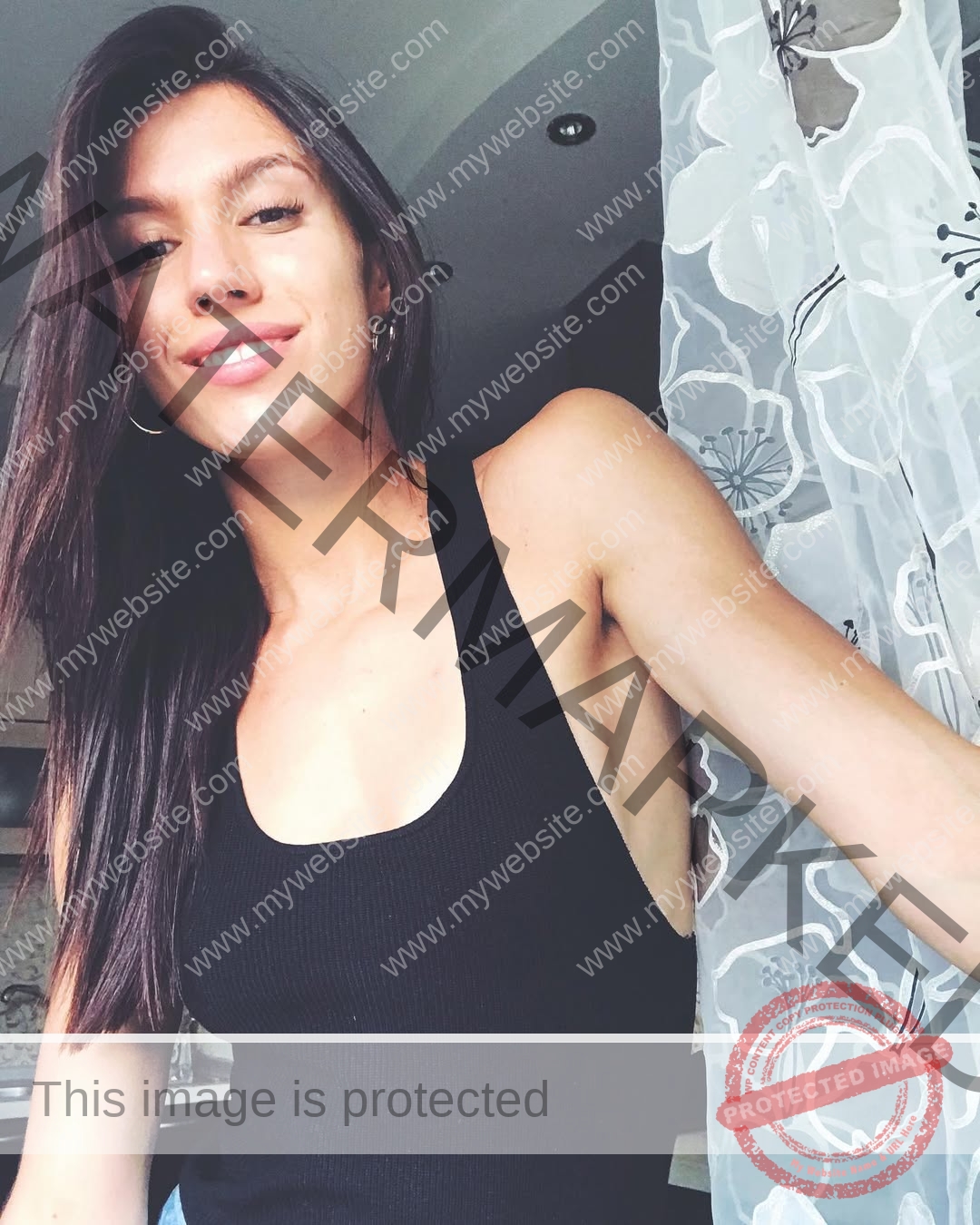 anastasia-bryzgina-ukraine-bryzgina_a-04143 Anastasia Bryzgina, track star from Ukraine, with long dark hair and a black sleeveless top, smiles by a window with a sheer floral curtain.