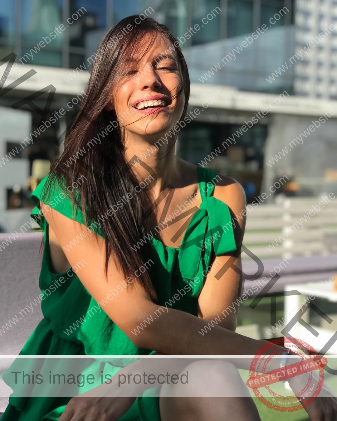 anastasia-bryzgina-ukraine-bryzgina_a-04150 Anastasia Bryzgina, track star from Ukraine, sits outdoors in a green dress, arms crossed and smiling in the sun near modern seating.