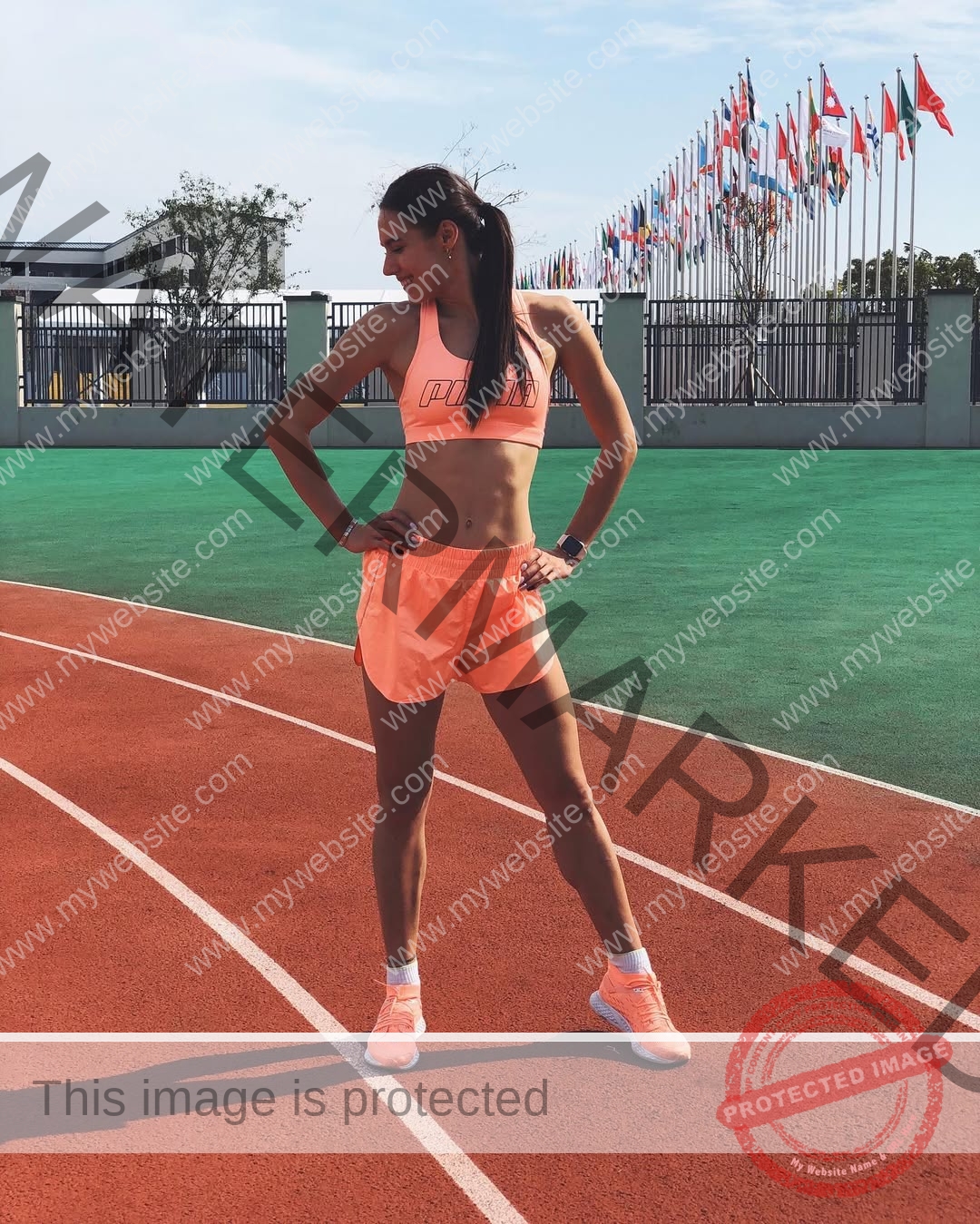 anastasia-bryzgina-ukraine-bryzgina_a-04164 Anastasia Bryzgina, track star from Ukraine, stands confidently on a red running track in peach athletic wear under a blue sky.
