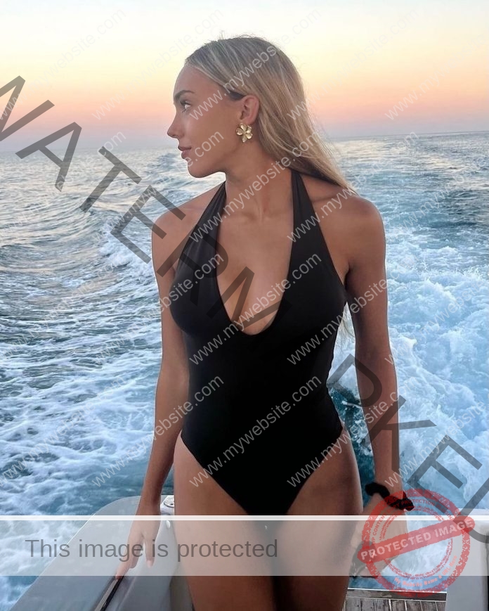Andrea De La Rosa, track star from Spain, stands on a boat in a black halter swimsuit at sunset, wearing gold flower earrings.