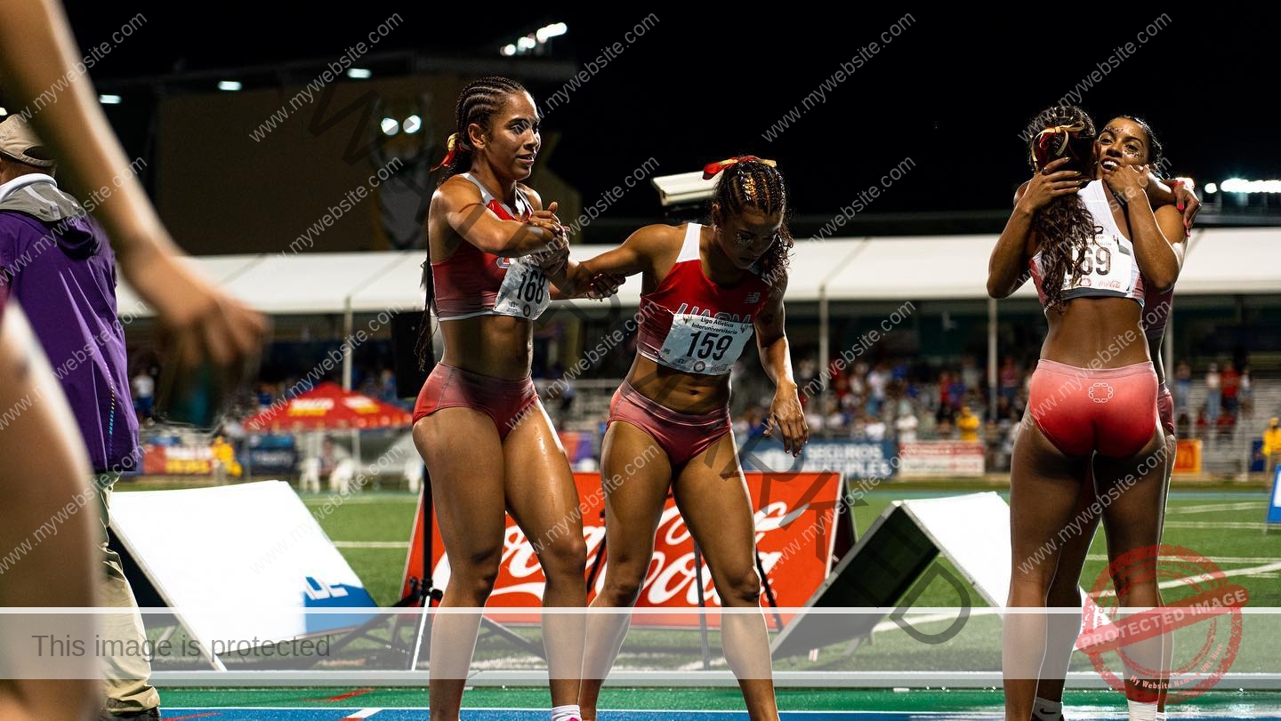 andrea-rivera-aviles-puerto-rico-aandrea.sofiaa-05888 Andrea Rivera Aviles, track athlete from Puerto Rico, celebrates on a stadium track at night with teammates in red uniforms; two hug, two high-five.