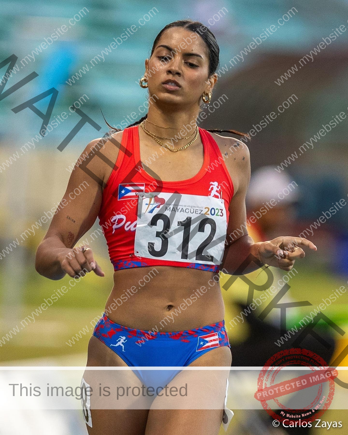 andrea-rivera-aviles-puerto-rico-aandrea.sofiaa-05892 Andrea Rivera Aviles, track athlete from Puerto Rico, in a red and blue uniform number 312 runs focused at Mayagüez 2023 games.