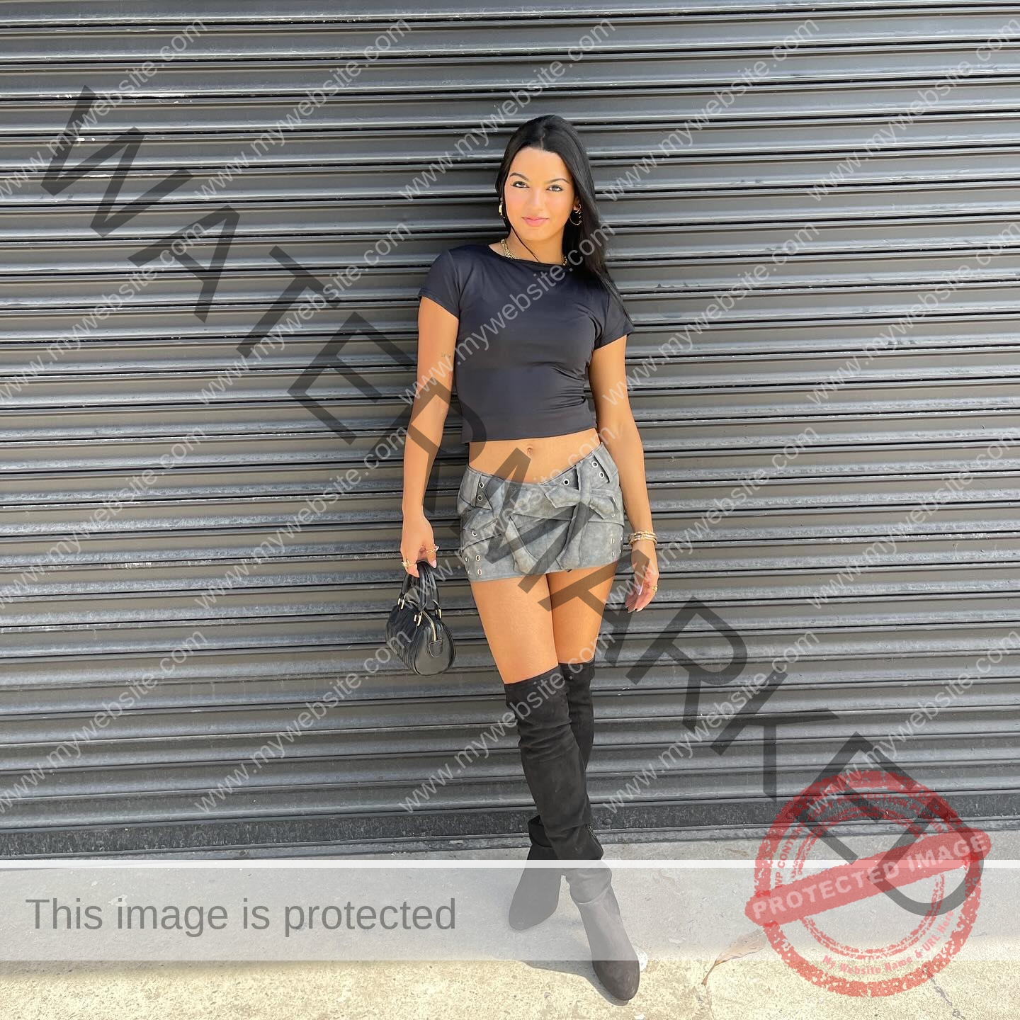 andrea-rivera-aviles-puerto-rico-aandrea.sofiaa-05902 Andrea Rivera Aviles, track athlete from Puerto Rico, stands by a metal shutter in a black crop top, gray skirt, boots, and smiles.