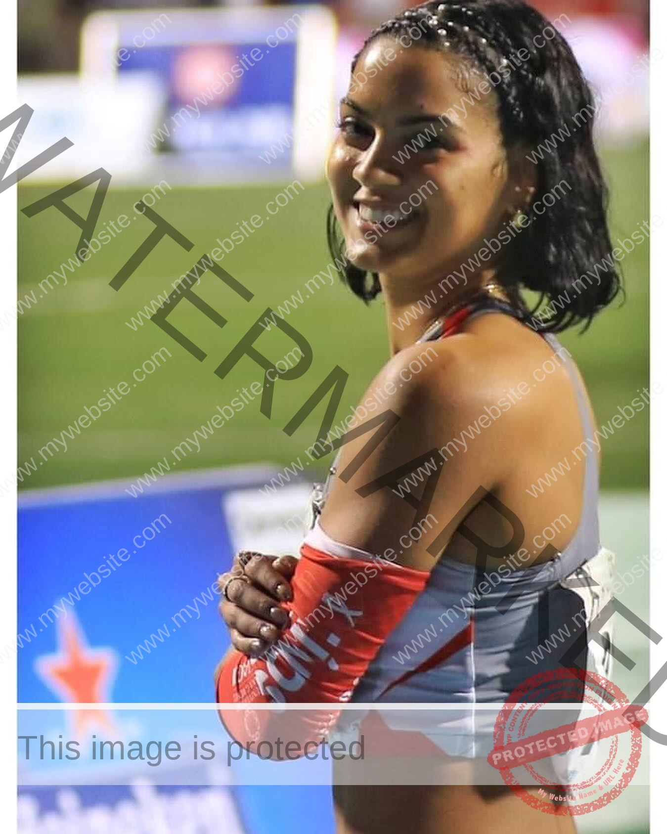 andrea-rivera-aviles-puerto-rico-aandrea.sofiaa-05907 Andrea Rivera Aviles, track athlete from Puerto Rico, with braided hair smiles on a sports field in grey and red athletic gear and red arm sleeve.