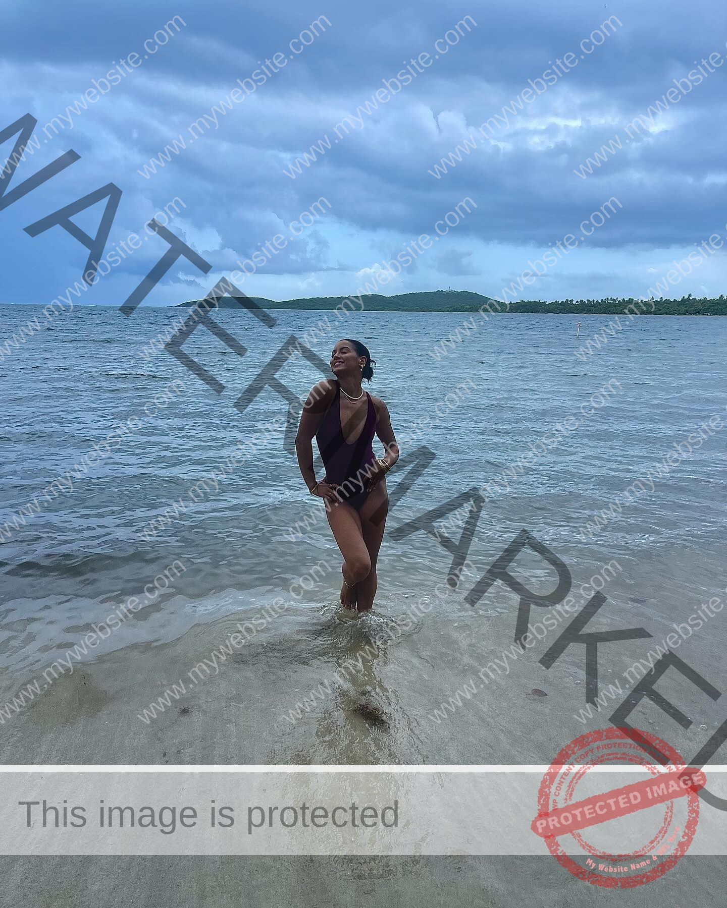 andrea-rivera-aviles-puerto-rico-aandrea.sofiaa-05909 Andrea Rivera Aviles, track athlete from Puerto Rico, stands at the shore in a black swimsuit, smiling as waves touch her feet.