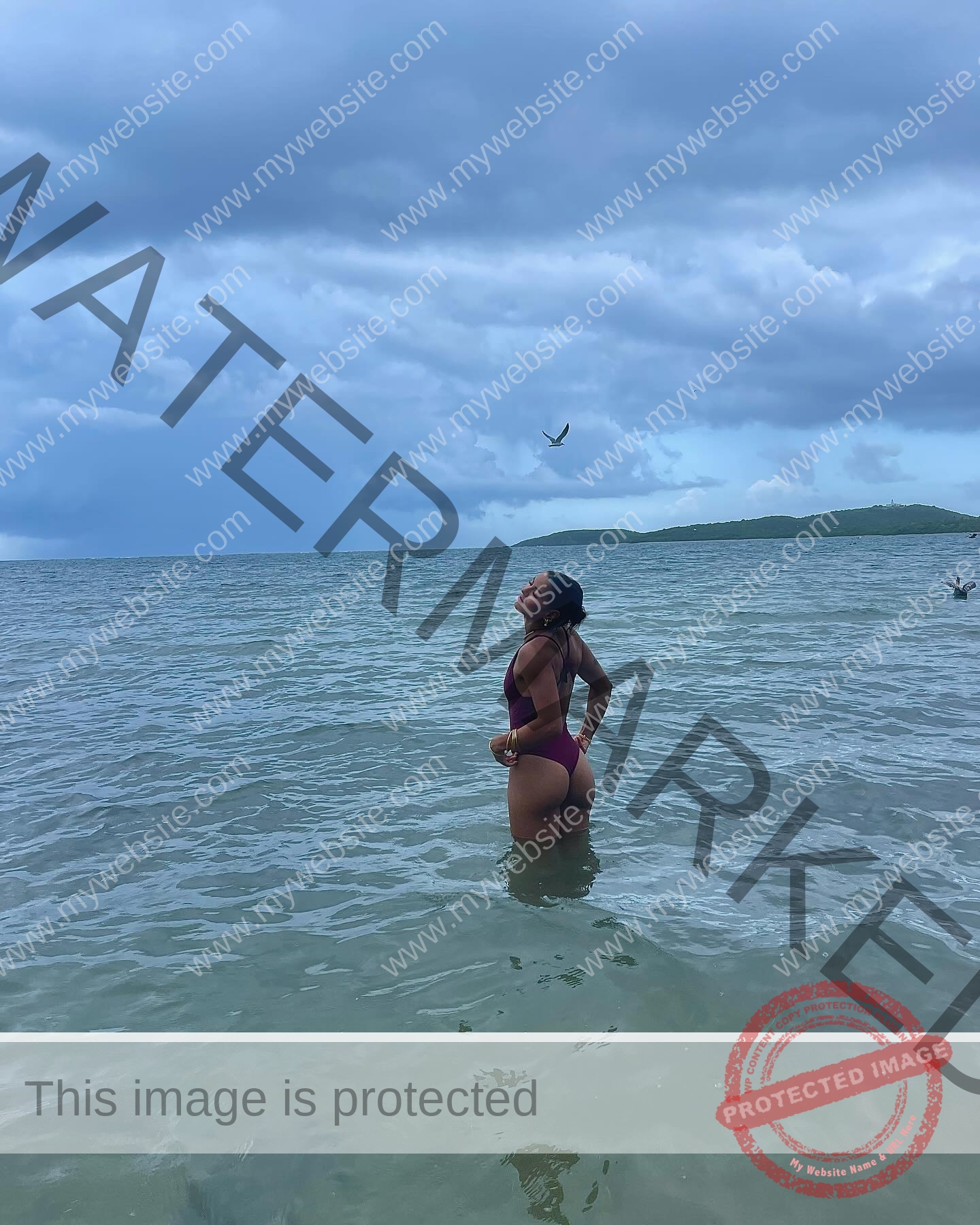 andrea-rivera-aviles-puerto-rico-aandrea.sofiaa-05910 Andrea Rivera Aviles, track athlete from Puerto Rico, stands waist-deep in the ocean gazing up as a bird soars above distant green hills.