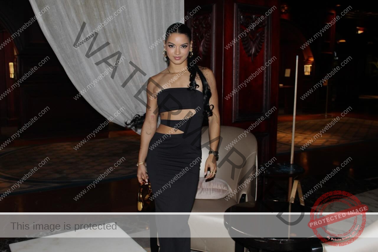 andrea-rivera-aviles-puerto-rico-aandrea.sofiaa-05923 Andrea Rivera Aviles, track athlete from Puerto Rico, poses indoors in a black cut-out dress by a beige chair and dark table.