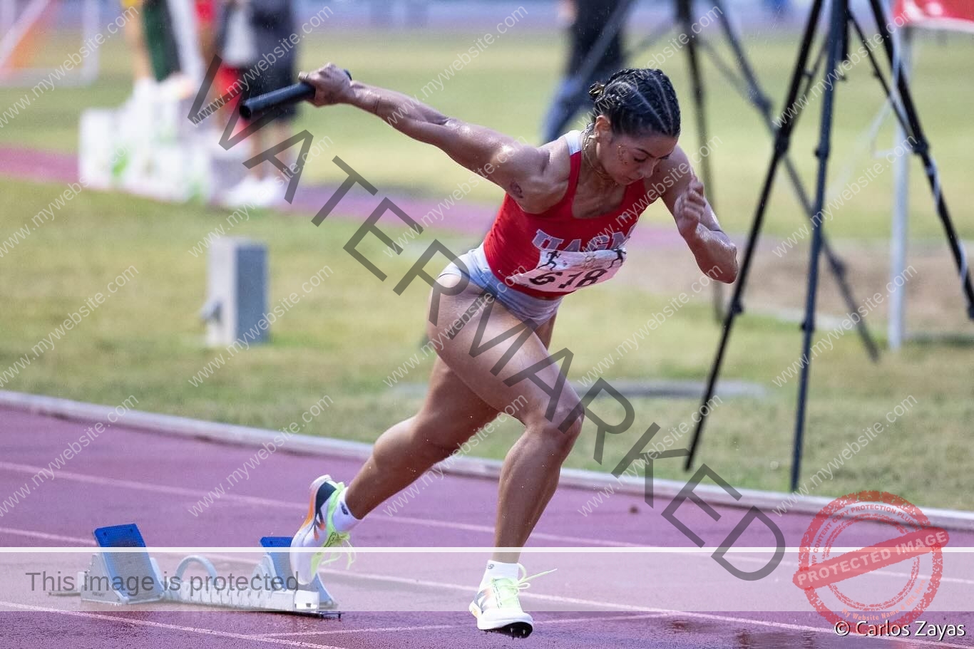 andrea-rivera-aviles-puerto-rico-aandrea.sofiaa-05929 Andrea Rivera Aviles, track athlete from Puerto Rico, sprints from starting blocks in red uniform, clutching relay baton on the track.