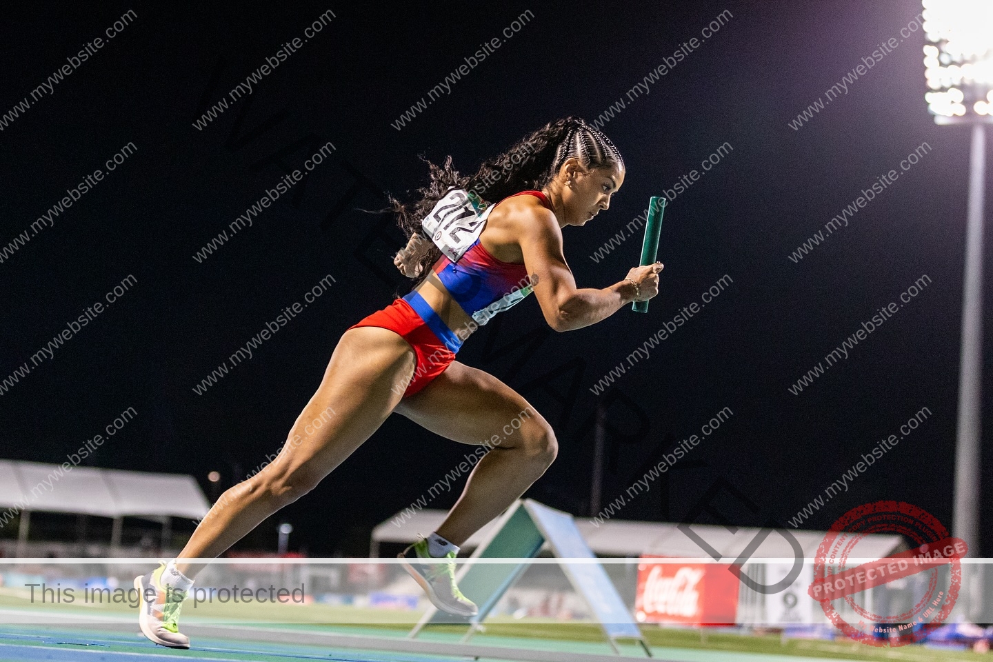 andrea-rivera-aviles-puerto-rico-aandrea.sofiaa-05933 Andrea Rivera Aviles, track athlete from Puerto Rico, sprints at night in red and blue with a relay baton under bright stadium lights.