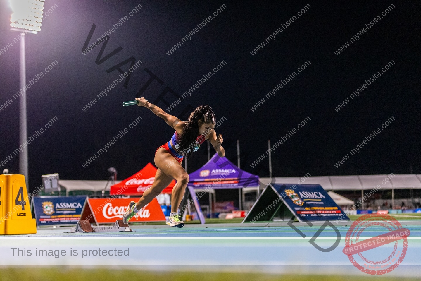 andrea-rivera-aviles-puerto-rico-aandrea.sofiaa-05934 Andrea Rivera Aviles, track athlete from Puerto Rico, starts a night relay race, launching off the blocks with baton on lit track.