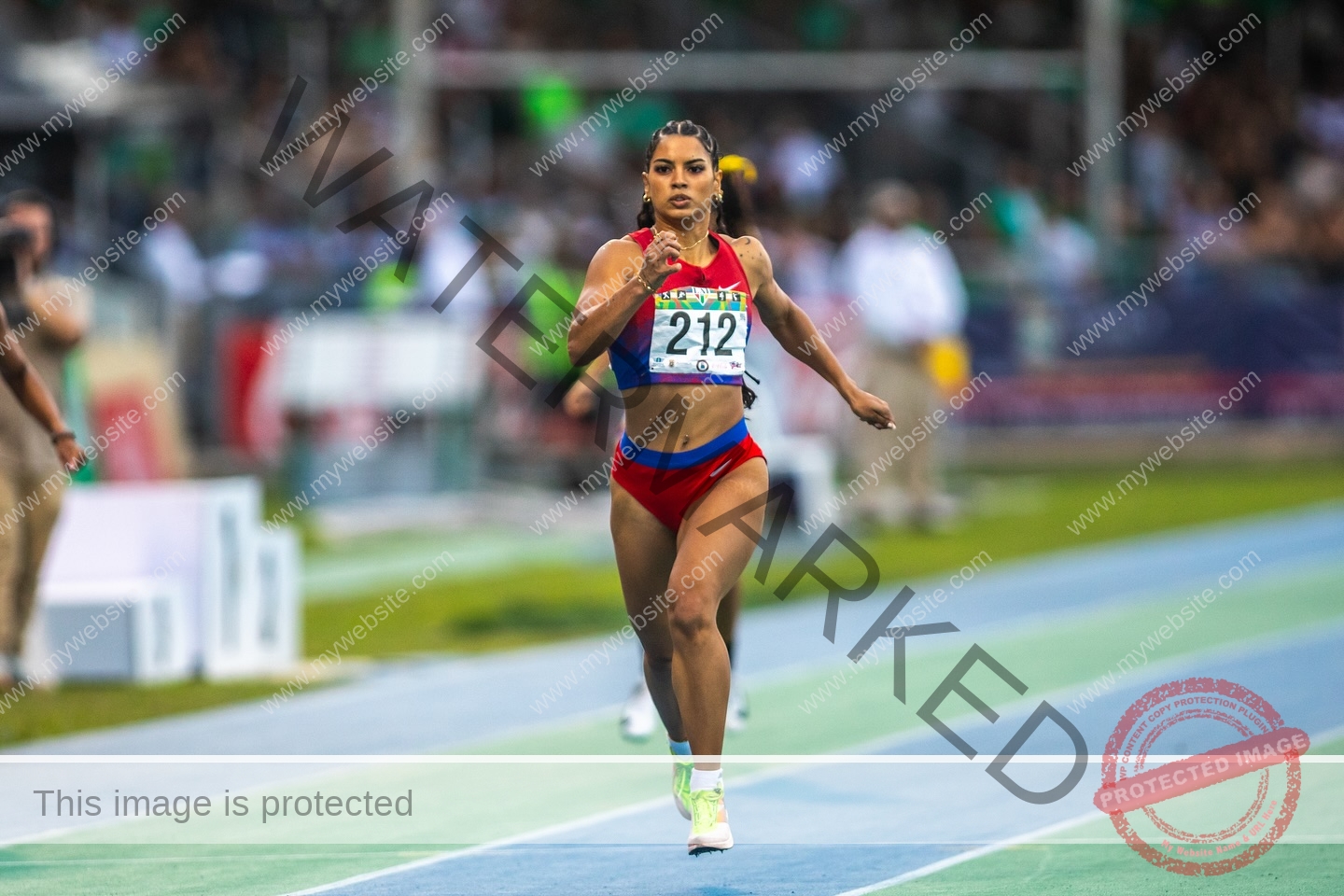 andrea-rivera-aviles-puerto-rico-aandrea.sofiaa-05940 Andrea Rivera Aviles, track athlete from Puerto Rico, wears red and blue number 212 sprinting on a track, spectators blurred behind.