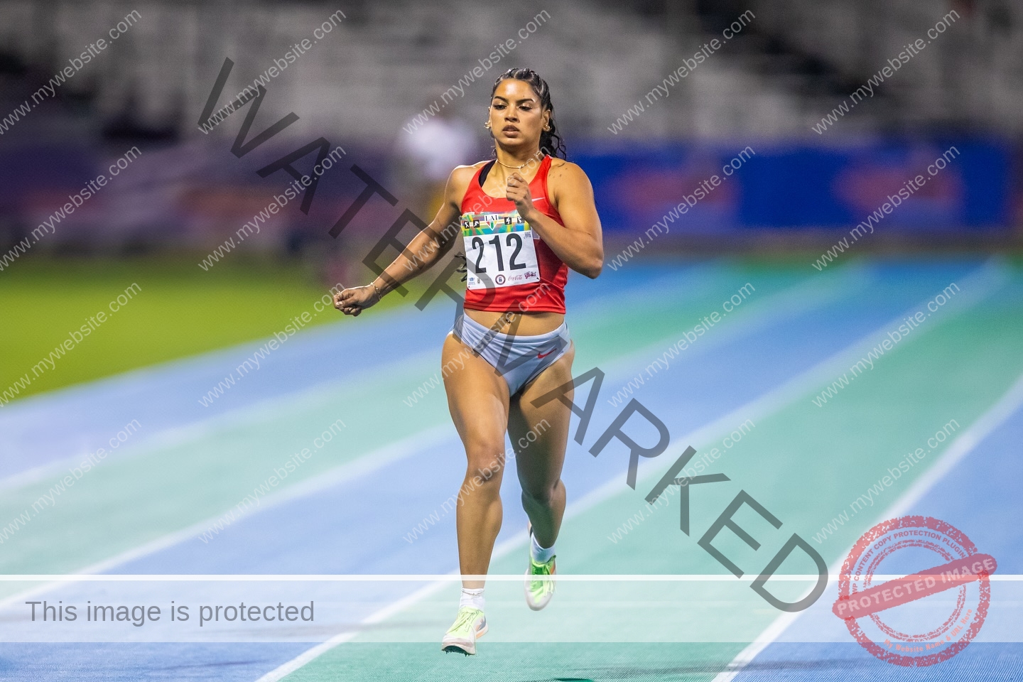 andrea-rivera-aviles-puerto-rico-aandrea.sofiaa-05943 Andrea Rivera Aviles, track athlete from Puerto Rico, sprints solo in red top and gray shorts, bib 212, on a blue-green track.
