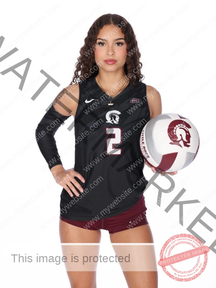 Andrea Roman, volleyball star from Puerto Rico, poses in a black and maroon uniform holding a Trojan-logo ball against a white background.