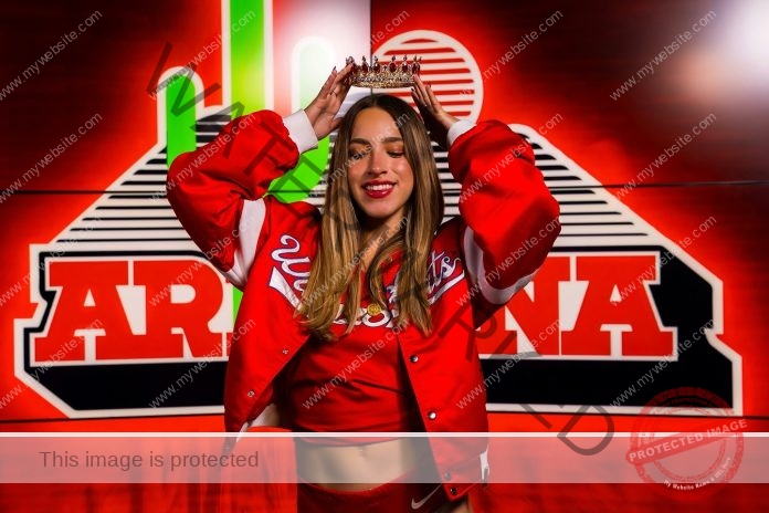 Antonia Sanchez Nunez Antonia Sánchez Núñez, dressed in red, smiles and crowns herself before an ARIZONA backdrop with a cactus—celebrating track and field achievements.