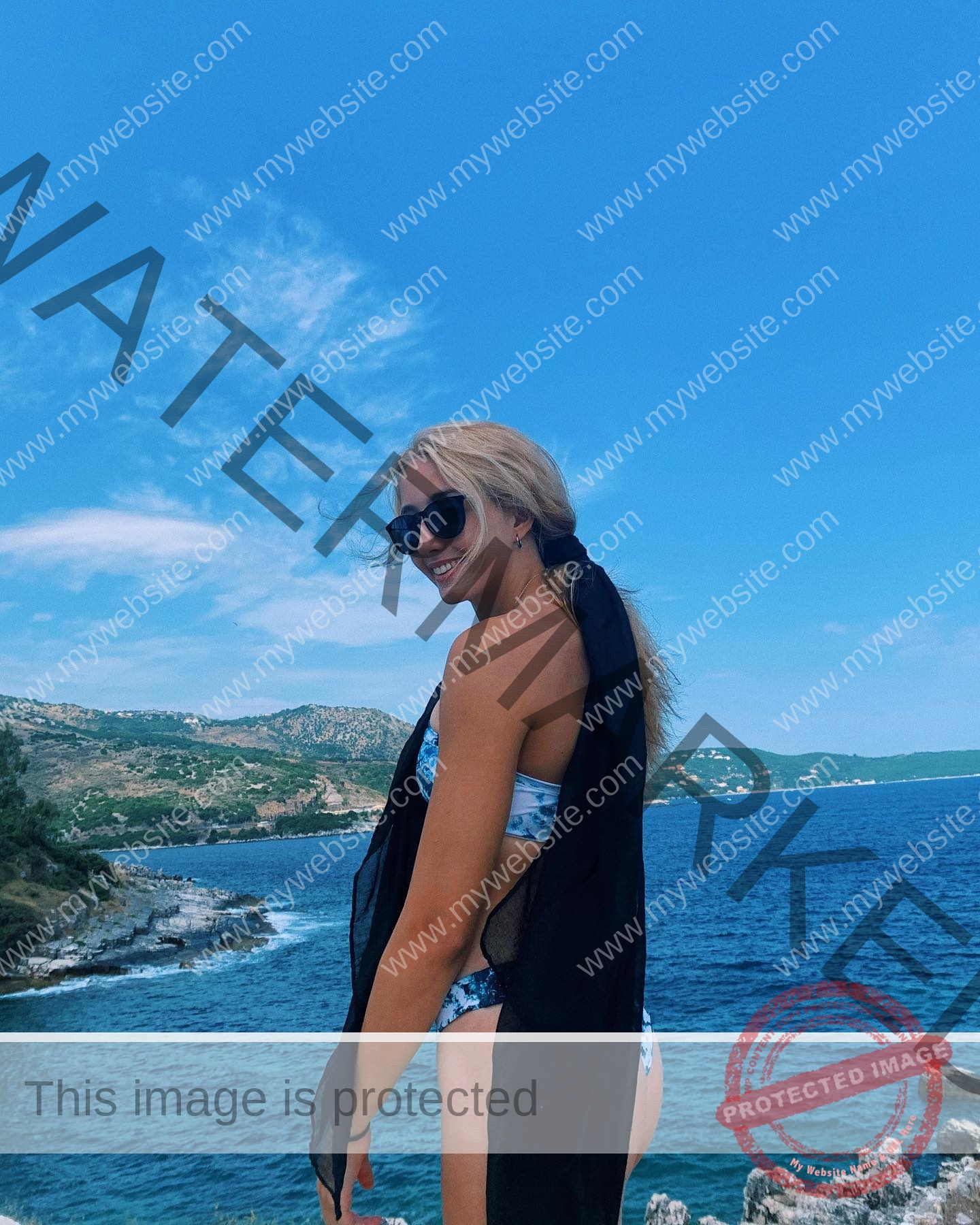 ariadni-adamopoulou-greece-ariadni_adam-08971 Ariadni Adamopoulou, pole vaulter from Greece and Oklahoma State, in a blue bikini and black scarf poses on a rocky coastline, smiling.