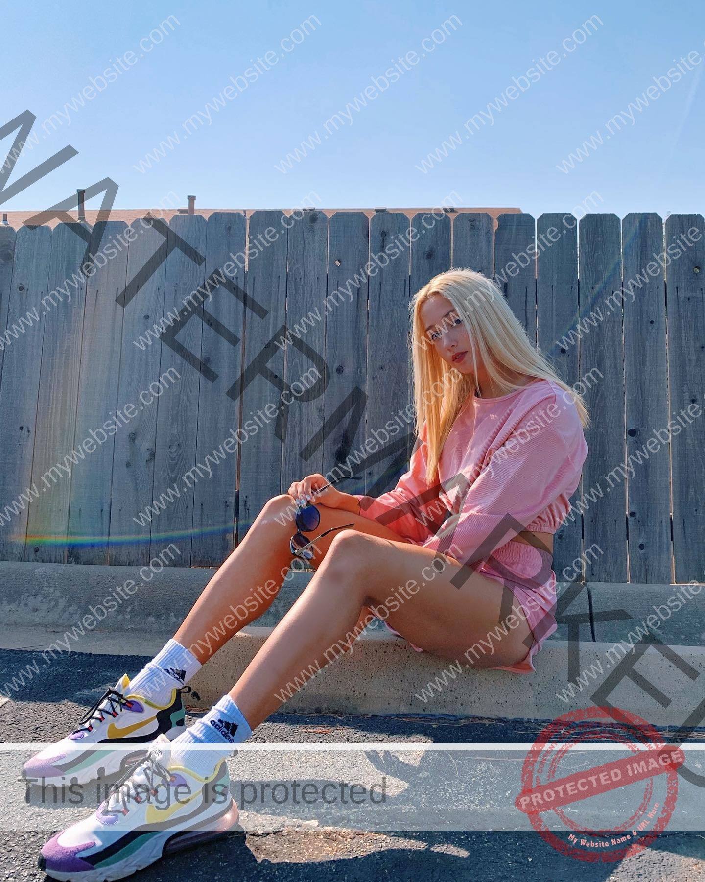 ariadni-adamopoulou-greece-ariadni_adam-08981 Ariadni Adamopoulou, pole vaulter from Greece and Oklahoma State, sits on a curb in pink clothes, holding sunglasses, looking ahead.
