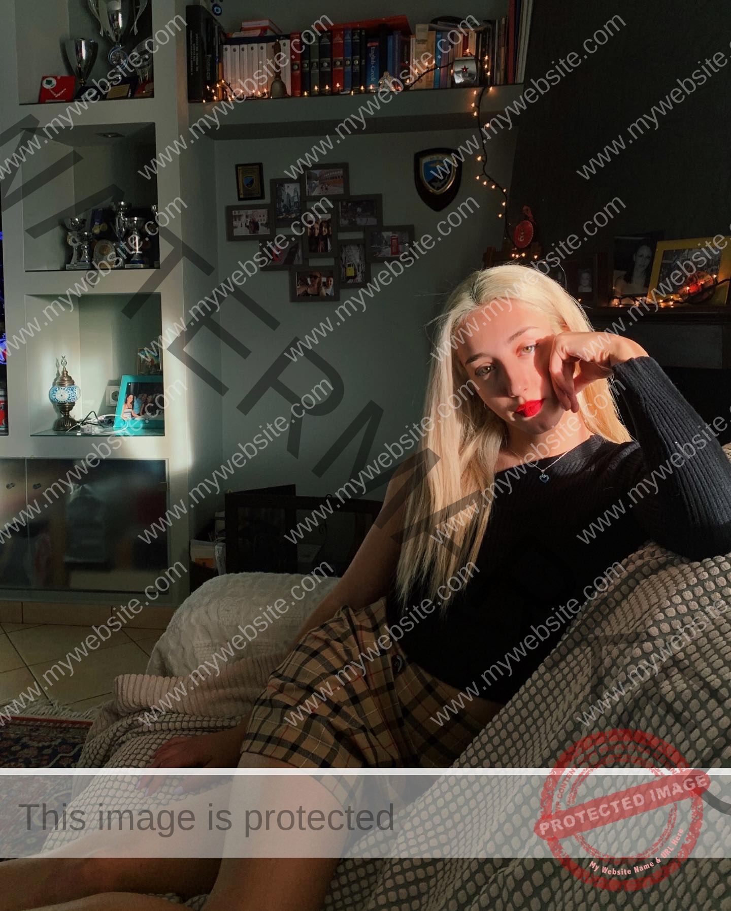 ariadni-adamopoulou-greece-ariadni_adam-08982 Ariadni Adamopoulou, pole vaulter from Greece and Oklahoma State sits on a couch in a cozy, softly lit room, gazing thoughtfully.