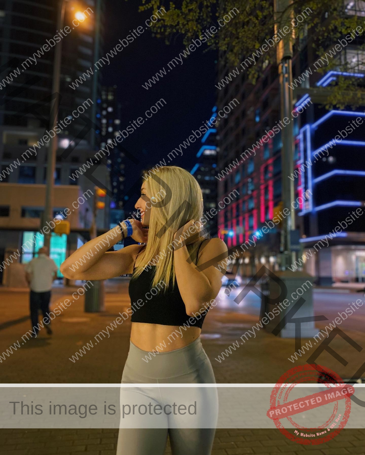 ariadni-adamopoulou-greece-ariadni_adam-08990 Ariadni Adamopoulou, pole vaulter from Greece and Oklahoma State, stands smiling on a city street at night in sporty attire.